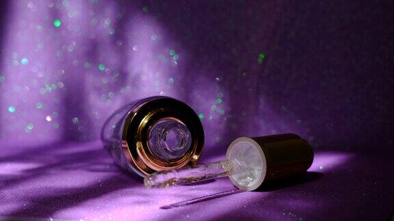 脸部美容油或精华液的特写透明滴瓶装饰花朵金色闪闪发光的紫色背景玻璃移液管中的玻尿酸