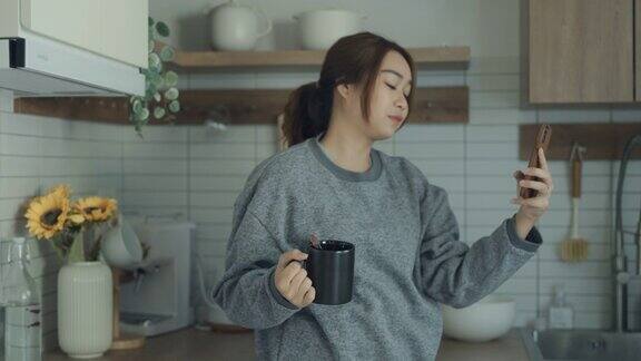 年轻的亚洲女性在家里的厨房餐具室使用手机