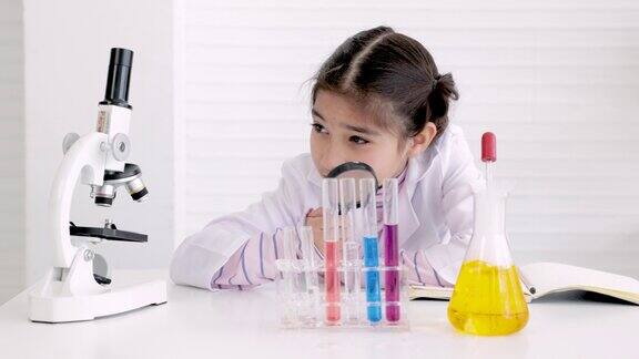 穿着长袍套装的科学小学女孩在化学教室里用放大镜看化学试管年轻的科学孩子在实验室里做实验