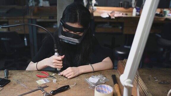 亚洲韩国女学生在大学工作台上用放大镜缝制珠宝