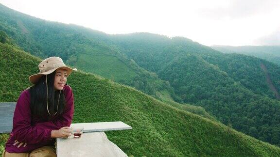 亚洲女人拿着咖啡杯和喝咖啡在山顶的背景慢旅行的生活方式与浸咖啡4k慢动作