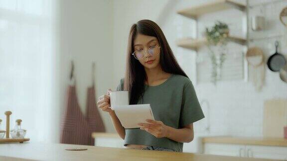 快乐的年轻亚洲女人戴着眼镜在厨房在家里女专心读书笔记做饭