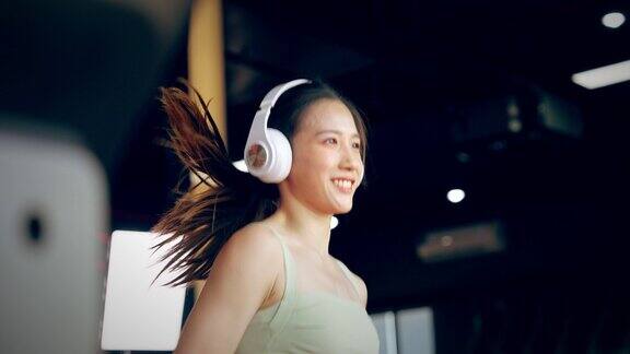 年轻的亚洲妇女戴着耳机在跑步机上跑步-健身健身房锻炼