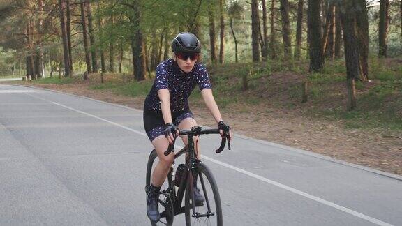 女孩骑着黑色的自行车穿着蓝色的运动衫和黑色的头盔在公园里骑为自行车比赛进行训练慢动作