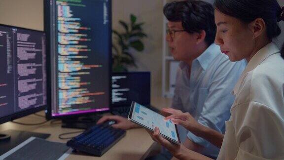 一群亚洲人软件开发人员晚上坐在办公室里有多个屏幕的办公桌前用电脑写代码程序员开发