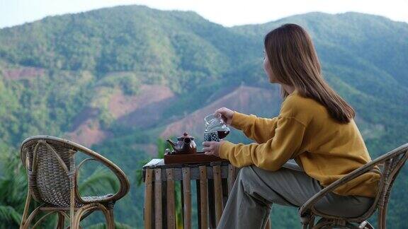 一个女人一边倒咖啡一边看着美丽的山景