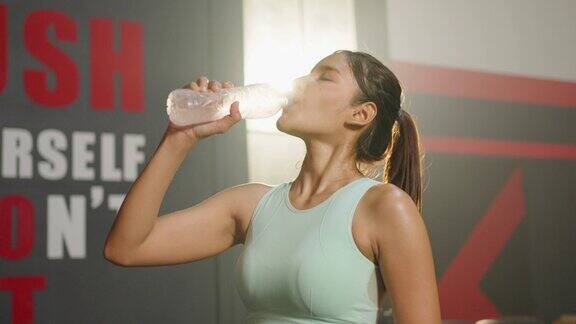 亚洲年轻的女运动员在健身房锻炼后喝一瓶水迷人的美丽的运动员女孩在健身馆锻炼时休息以保持肌肉的保健和幸福