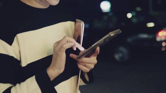 亚洲女人晚上在城市街道上用智能手机发短信