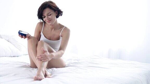 身体皮肤护理女人在卧室用身体霜擦腿皮肤