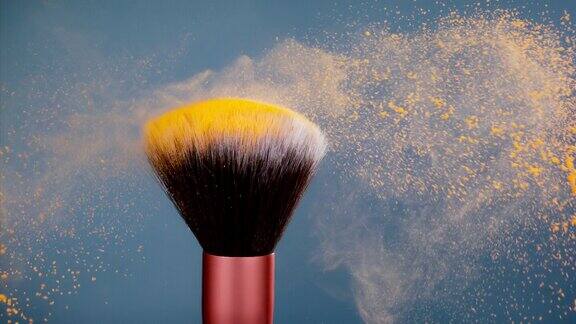 化妆刷与黄色粉末爆炸在蓝色背景超级慢动作