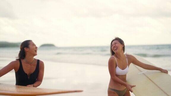 4K亚洲女性肖像在阳光明媚的日子里拿着冲浪板一起走在沙滩上