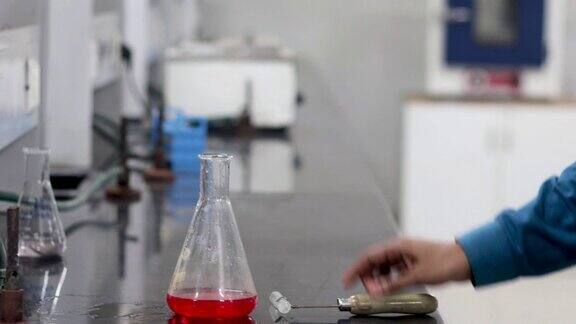 一个研究科学家的手从一个试管倒入一个红色的化学物质在一个锥形瓶