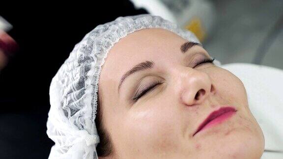 在脸部护理程序前美容师用湿棉垫清洁女性皮肤