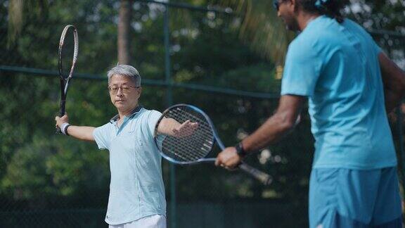 周末上午在网球场上亚洲华人老男子向网球教练学习