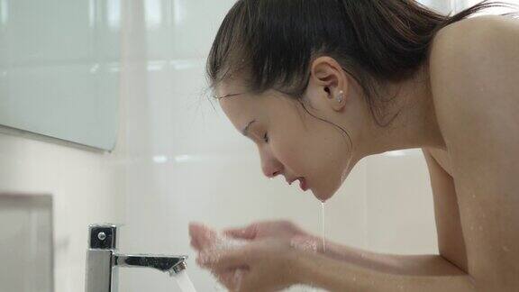 一名年轻女子在家里的浴室里洗脸
