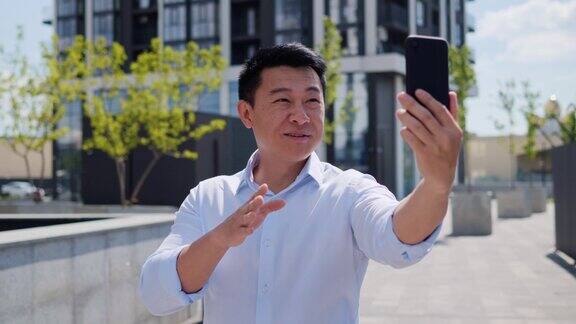 亚洲商人有在线视频电话微笑步行城市使用手机英俊的中国男性站在商业区的户外拍摄商人博主肖像的视频