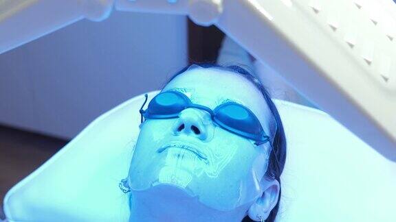 年轻女性面部敷胶原水凝胶面膜在美容院进行蓝光LED光面部治疗美丽和健康