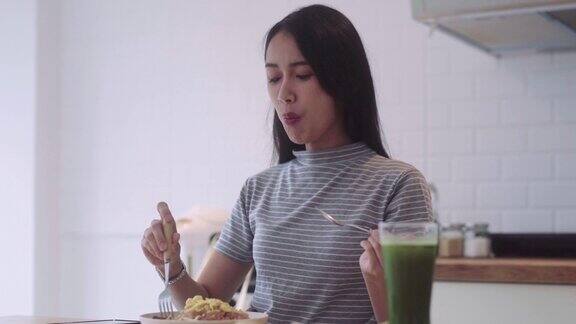 快乐餐亚洲妇女拿着叉子和勺子吃亚洲食物在盘子和桌子上的米饭在家里的厨房享受真正的异国情调自制健康泰餐