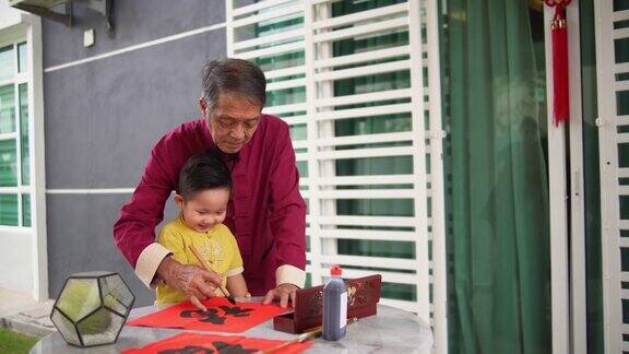 亚洲华人微笑的爷爷和孙子在中国新年期间在前院手写中国书法