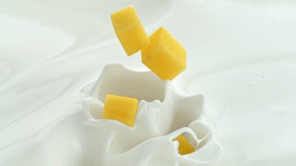 芒果块落入奶油牛奶中在微距和慢镜头中产生漩涡飞溅