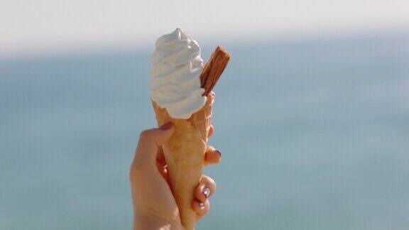 靠近手女子拿着冰淇淋香草口味的甜点在美丽的阳光海滩享受暑假吃软服务