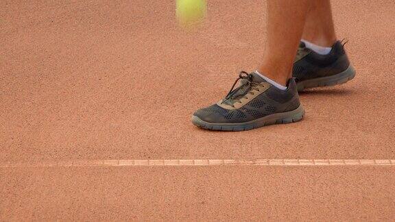 一名网球运动员在红土场上用他的网球鞋擦过底线弹起网球并发球的特写镜头