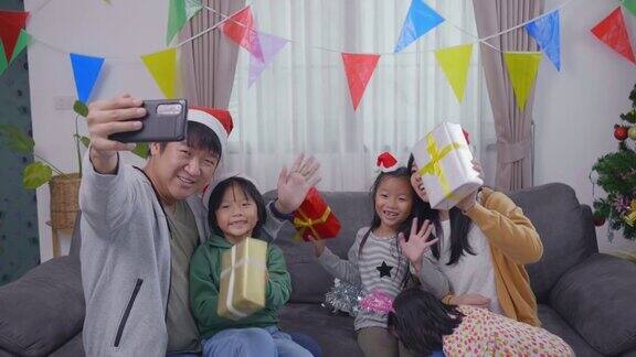 亚洲幸福家庭在圣诞节期间享受礼品盒和使用手机视频通话