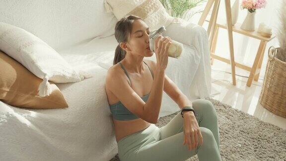 年轻的亚洲女运动员在家里的客厅里喝着蛋白质奶昔饮食和健康食品