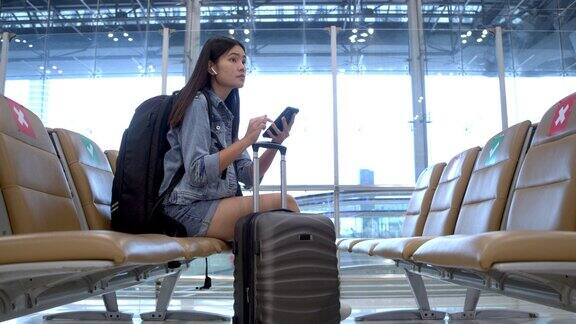 一个亚洲女人在等待航班用手机她把带轮子的行李箱拖进了客运大楼