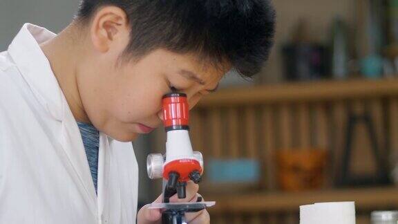 亚洲男孩穿着实验服在学校实验室使用显微镜进行测试教育的生活方式理念