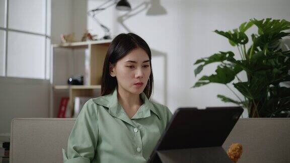 亚洲年轻女子在家边吃炸鸡边用平板电脑