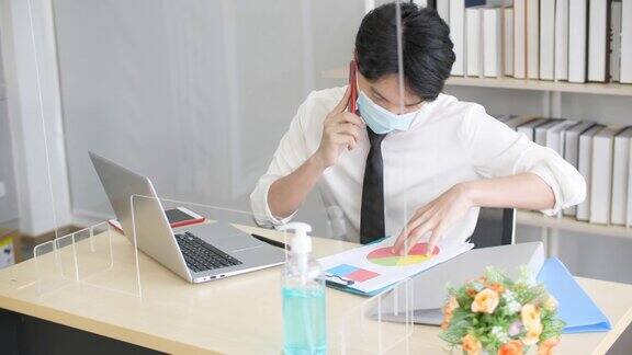 新常态办公室生活年轻人工作时戴口罩和玻璃墙预防病毒