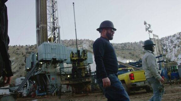 几个男性油田工人在一个寒冷的冬天的早晨走过一个石油和天然气钻井平台的慢镜头