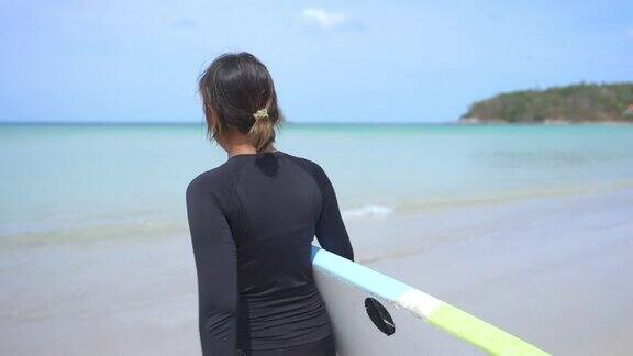 亚洲女人在莽撞的警卫手持冲浪板在海滩上行走