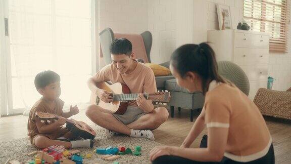 家庭学习:亚洲父子在音乐中寻找快乐微笑着弹吉他