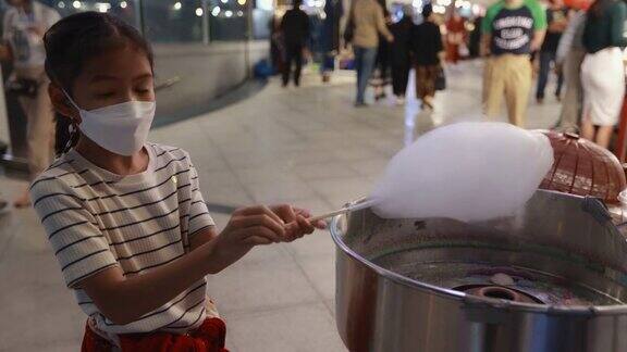 一个亚洲小女孩在街头夜市用特殊的机器制作棉花糖孩子们拿着一根棉花糖棒棉花糖棒上缠绕着细长的线