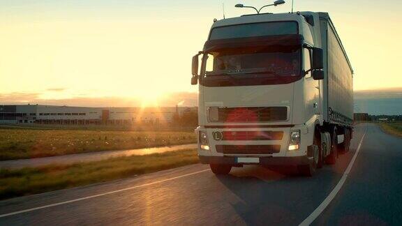 前视摄像头跟踪半卡车与货运拖车在高速公路上行驶他在夕阳的背景下快速穿过工业仓库