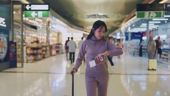 亚洲女性带着她的轮式行李走在机场用智能手机看手表的时间