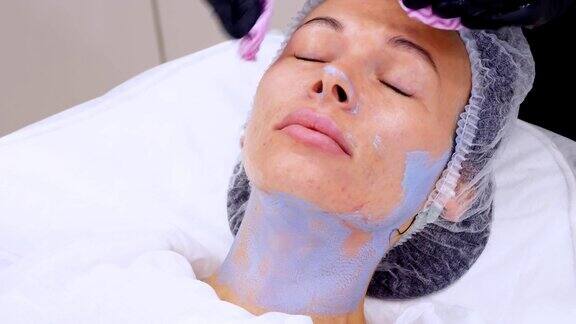 特写化妆师在黑色医疗手套去除化妆品面膜的残余从女性脸上用特殊的湿巾在美容诊所或美容院进行皮肤护理