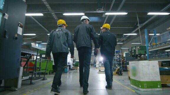 后视图高级工程师和两个工人正在走过工厂空间的文件