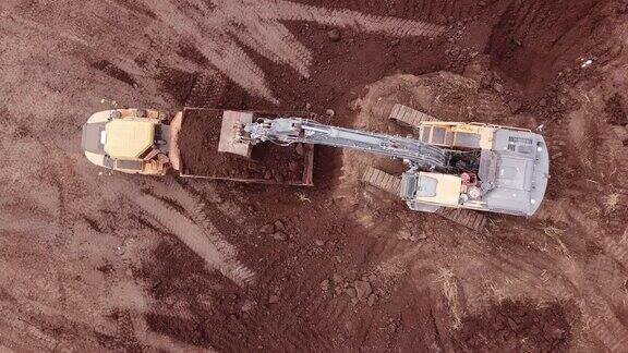 挖掘机在自卸卡车上装载泥土土方设备鸟瞰图