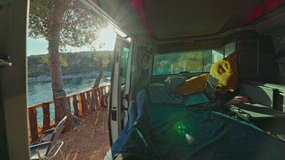 男人坐在他的面包车里伸开双腿夕阳在地平线上面包车的门打开了阳光面包车的生活
