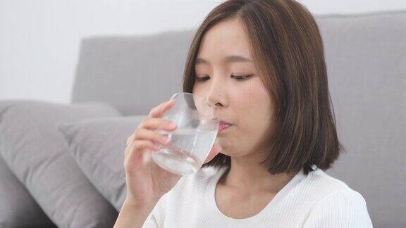 年轻的亚洲女子坐在家里的客厅里喝淡水