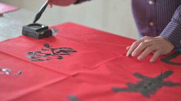 亚洲华人男性练习书法为即将到来的中国新年庆祝家庭装饰目的与繁荣和良好的措辞写在一张红色的纸上