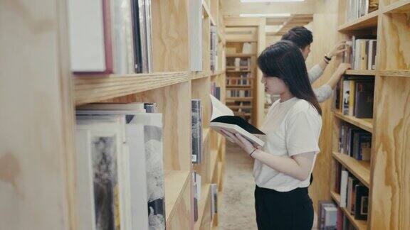 年轻的亚洲大学生在图书馆找书(慢镜头)