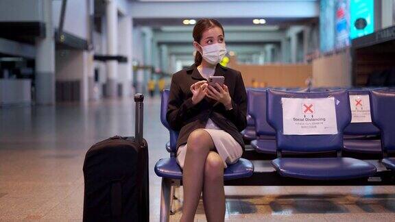 亚洲人戴着口罩坐在机场距离他人一个座位的地方保持距离防止感染COVID-19病毒