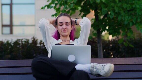 一个年轻漂亮的女学生坐在校园长凳上拿着一台笔记本电脑一位黑发长发的女性在工作之余在户外休息