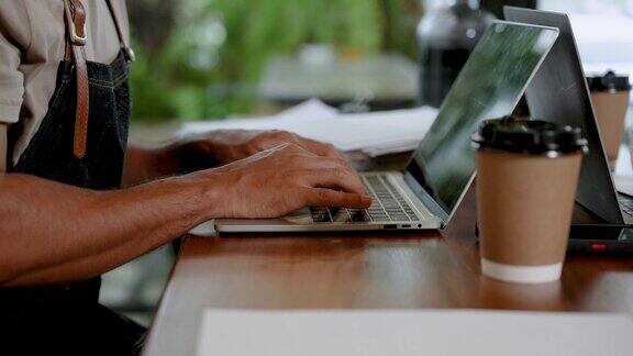 黑皮肤男子使用笔记本电脑的手特写创建一个小的业务收入和支出账户用手在电脑键盘上打字在咖啡馆的文件里打字