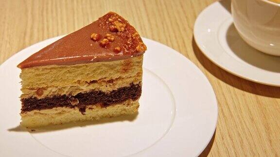 一块美味的焦糖蛋糕配巧克力和坚果在咖啡馆的木桌上吃一块甜蛋糕和一杯牛奶卡布奇诺咖啡美味的蛋糕放在白色盘子上甜点叉子