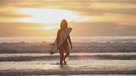 夕阳下的热带海滩上冲浪女孩的剪影